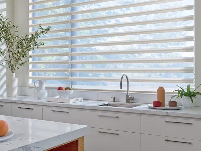A kitchen with hard surfaces and soft window coverings.